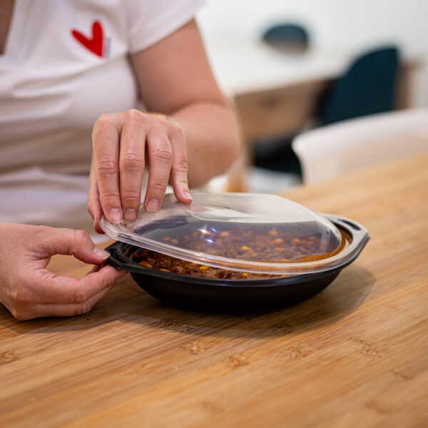 Jeune maman en train d’ouvrir un contenant plastique réutilisable contenant un chili con carne, prêt à être réchauffé.